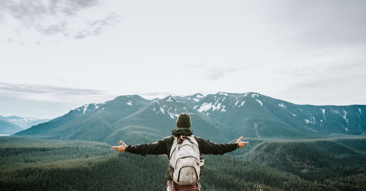 hiker with arms stretched looking at a mountain range