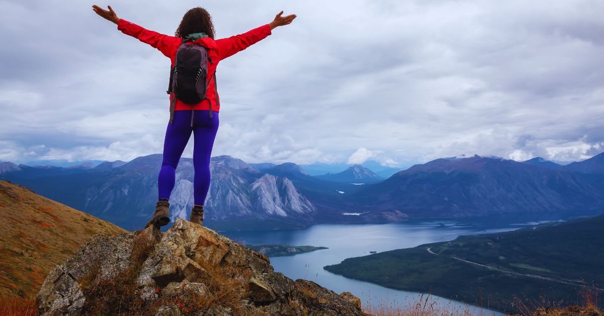 hiker standing on top of a rock with arms stretched